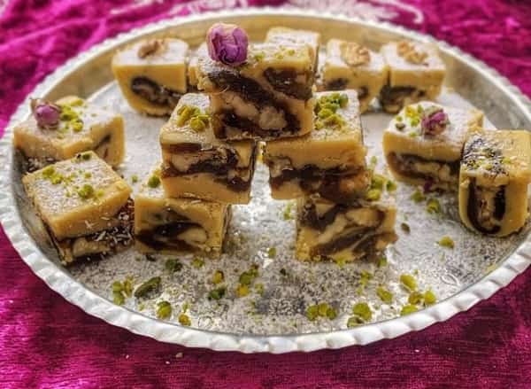 طرز تهیه رنگینک خرما بوشهری اصل چیست؟ با آردنخودچی و روغن مایع و گردو شیر خشک درست میشود .